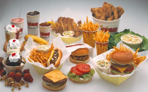 A variety of fast food items including burgers, fries, chicken, salads, and desserts arranged on a table.