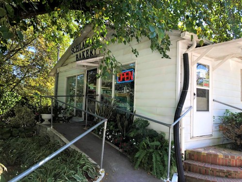 A charming white bakery with an "OPEN" sign, surrounded by greenery and a welcoming entrance.