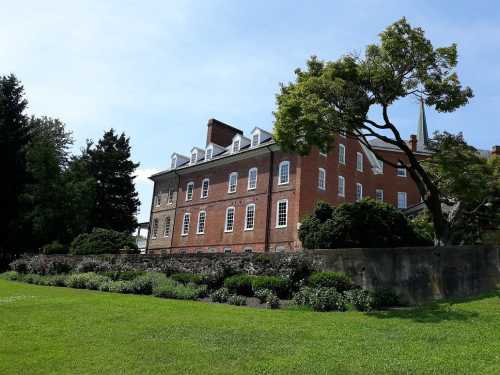 A historic brick building surrounded by lush greenery and trees under a clear blue sky.