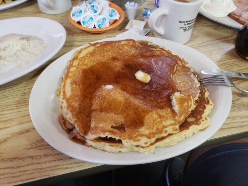 A large stack of golden pancakes topped with butter and syrup, served on a white plate.