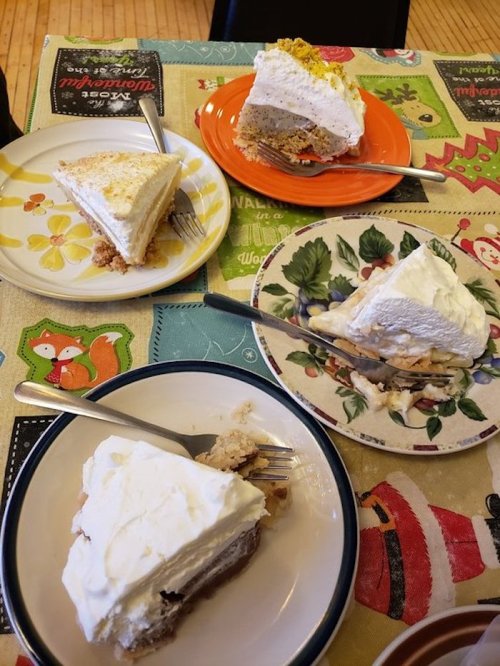 Four slices of different cakes on colorful plates, with forks resting beside them, on a festive tablecloth.