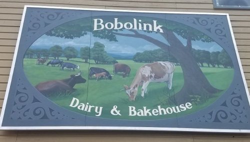 Sign for Bobolink Dairy & Bakehouse featuring cows grazing in a green field under a tree.