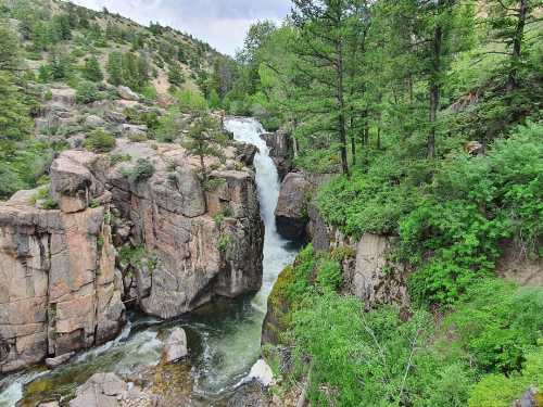 A scenic waterfall cascading through rocky cliffs, surrounded by lush green trees and a cloudy sky.