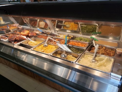 A buffet display featuring various dishes, including meats, sides, and sauces in metal trays with serving utensils.
