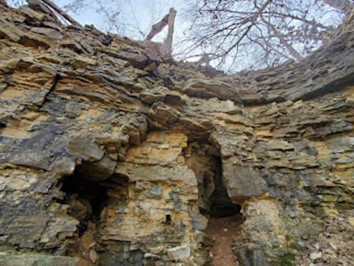 Rocky cliffside with weathered stone formations and sparse trees above, under a clear sky.