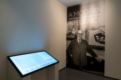 Exhibition space featuring a large portrait of a man and a display table with information about modern art influences.