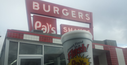 A cup from Pal's Shakes in front of a red and white burger restaurant sign.