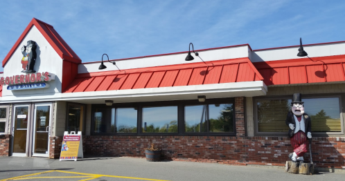 Exterior of a restaurant with a red roof, featuring a cartoonish statue in front and large windows.