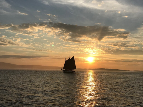 A silhouette of a sailing ship against a vibrant sunset over calm waters.