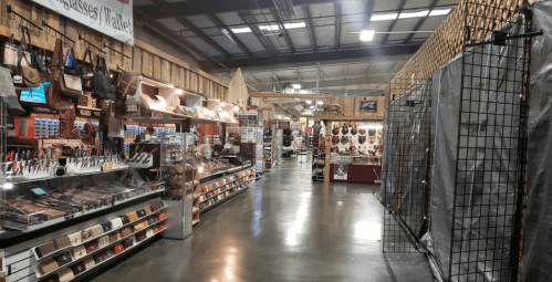 A spacious indoor market aisle lined with various bags, accessories, and displays on both sides.