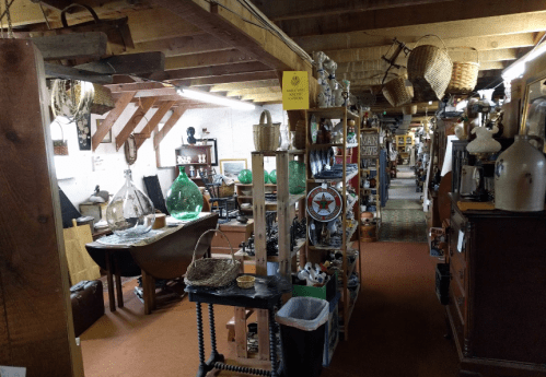 A cozy antique shop filled with various vintage items, shelves, and decorative objects under wooden beams.