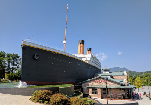 A large replica of the Titanic stands next to a brick building under a clear blue sky.