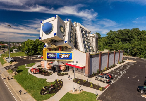 A quirky building shaped like a giant camera lens, with a blue and white design, surrounded by a parking lot and trees.