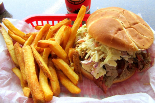 A hearty sandwich filled with meat and coleslaw, served with a side of golden French fries in a red basket.