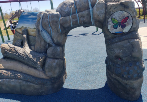A textured stone archway at a playground, featuring a butterfly design and surrounded by colorful play equipment.