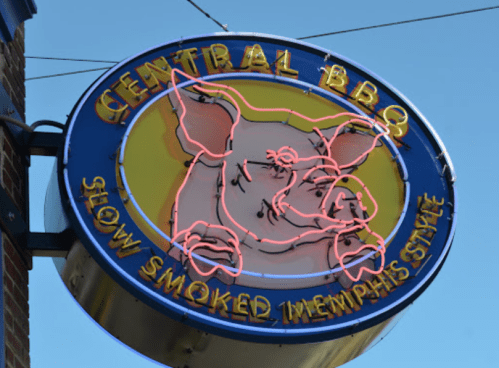 Neon sign for Central BBQ featuring a pig graphic and the text "Slow Smoked Memphis Style" against a blue sky.