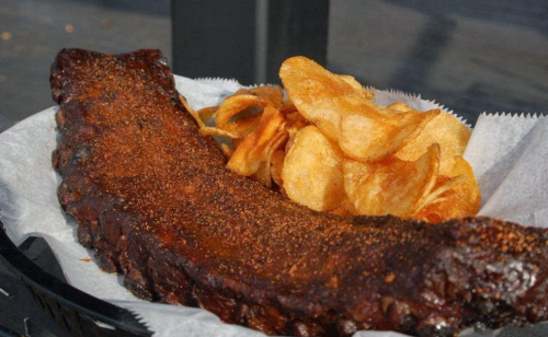 A plate featuring a smoky, seasoned rib alongside a serving of crispy potato chips.