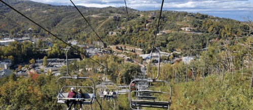 A scenic view from a chairlift, overlooking a lush green hillside and a small town below.