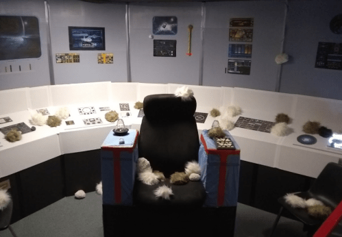 A sci-fi themed room with a central black chair, control panels, and fluffy decorations scattered around.
