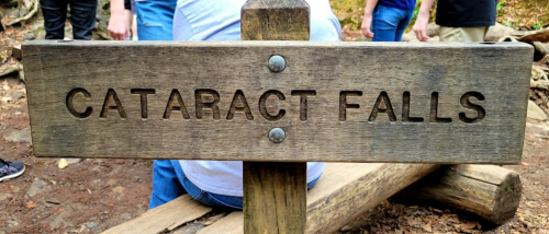 Wooden sign reading "Cataract Falls" in a natural setting, with people in the background.