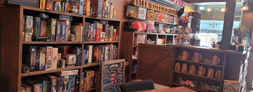 A cozy game café with shelves filled with board games and a counter displaying snacks and drinks.