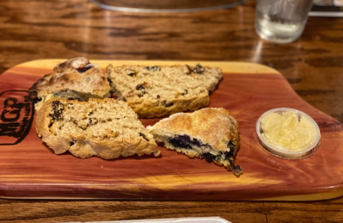 A wooden board with sliced bread, featuring dark fruit, and a small container of butter or spread on the side.