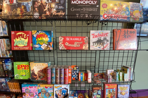 A display shelf filled with various board games, including Clue, Monopoly, Scrabble, and Catan.
