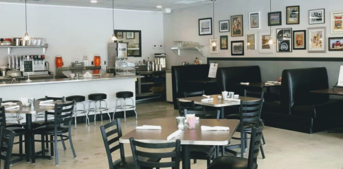 A cozy diner interior with black booths, tables, and a counter adorned with vintage photos on the walls.