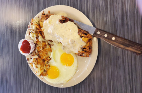 A plate of breakfast featuring two sunny-side-up eggs, hash browns, chicken fried steak, and gravy with a side of ketchup.