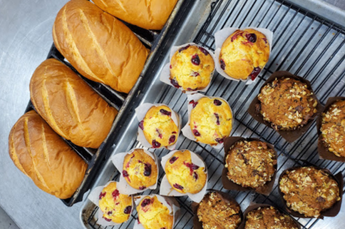 Freshly baked bread loaves and assorted muffins cooling on a wire rack.