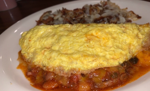 A plate featuring a fluffy omelette over a bed of beans and a side of crispy hash browns.