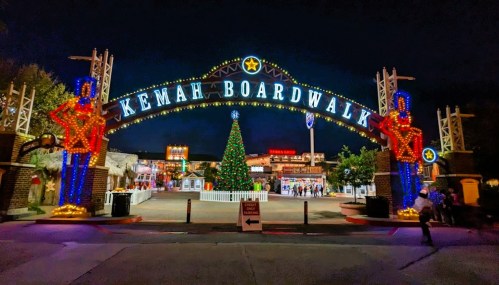Colorful holiday lights adorn the Kemah Boardwalk entrance, featuring a Christmas tree and festive decorations at night.