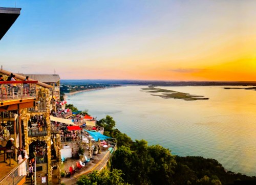 A scenic view of a river at sunset, with vibrant colors and people enjoying a lively atmosphere on a terrace.