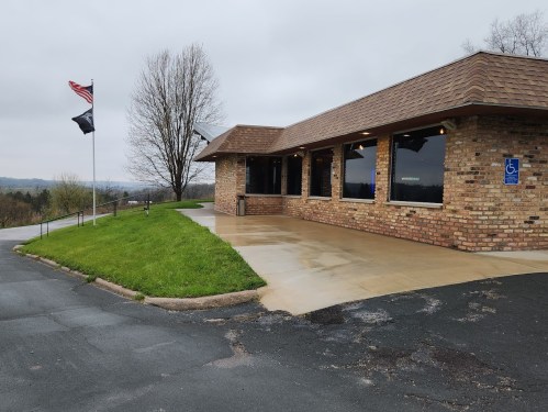 A brick building with a sloped entrance, flags flying, and a grassy area, set against a cloudy sky.