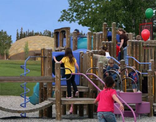 Children playing on a colorful playground with slides and climbing structures, surrounded by trees and balloons.