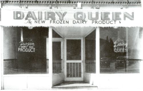 Black and white image of a Dairy Queen storefront with large signage and windows displaying "Frozen Dairy Product."