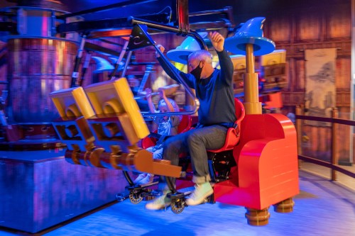 A person enjoys a ride on a colorful amusement attraction, arms raised in excitement, with a child beside them.