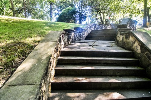 Stone steps lead up through a lush green park, surrounded by trees and dappled sunlight.