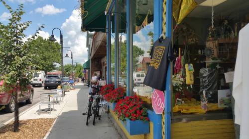 A vibrant street scene with flower boxes, bicycles, and shops under a sunny sky, showcasing a lively small-town atmosphere.