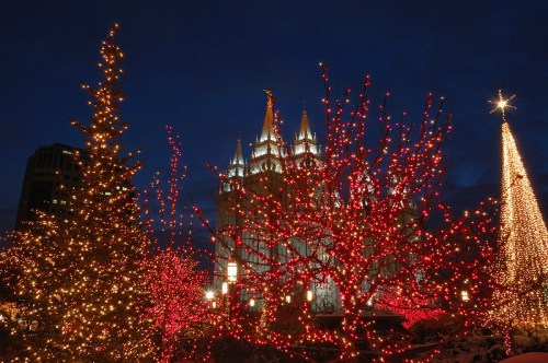 A festive scene featuring a lit-up temple surrounded by trees adorned with red and white Christmas lights at night.