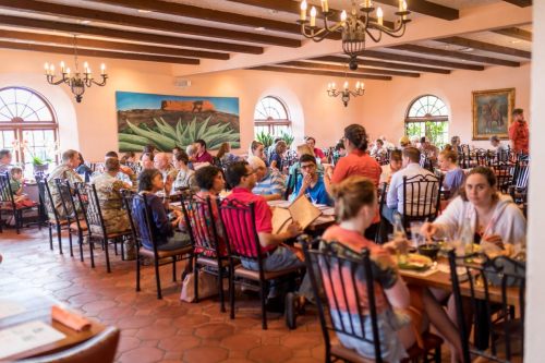 A busy restaurant filled with diners at tables, featuring warm decor and a large mural on the wall.