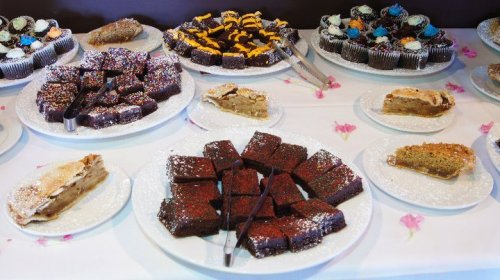A variety of desserts on white plates, including brownies, cupcakes, and slices of pie, decorated with sprinkles.