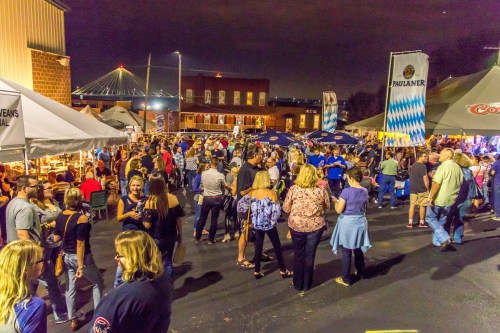 A lively night market scene with crowds, tents, and festive lights, set against a city backdrop.