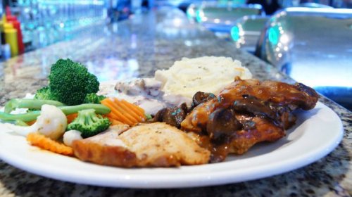 A plate of grilled chicken with mushroom sauce, mashed potatoes, and mixed vegetables on a countertop.