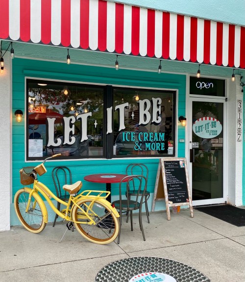 A colorful ice cream shop with a bright blue exterior, a yellow bike, and a sign reading "Let It Be Ice Cream & More."