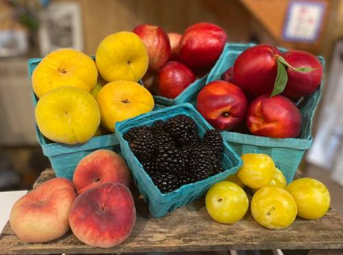 A colorful display of peaches, nectarines, and blackberries in blue baskets on a wooden surface.