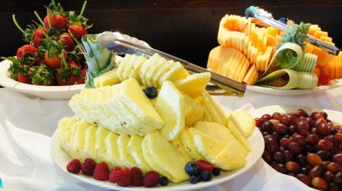 A colorful fruit display featuring sliced pineapple, strawberries, grapes, and melon arranged on white tablecloth.