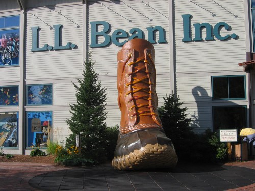 Giant boot sculpture in front of L.L. Bean store, surrounded by greenery and a clear blue sky.
