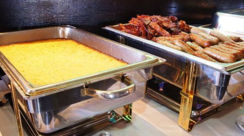 Two chafing dishes: one with cornbread and the other with bacon and sausage links.