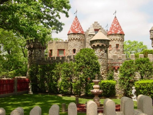 A whimsical stone castle with red-tiled turrets, surrounded by lush greenery and a manicured lawn.